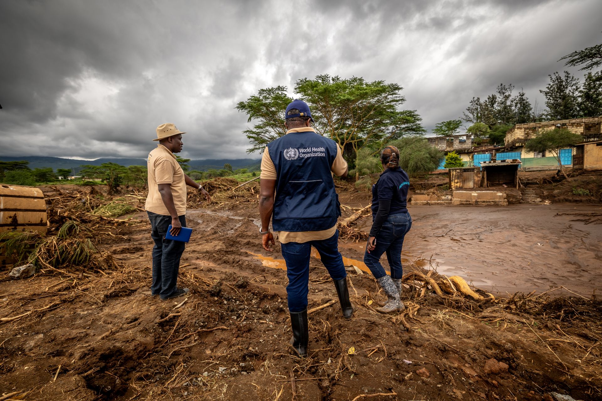 Man in WHO jacket and two other people looking over waterlogged ground